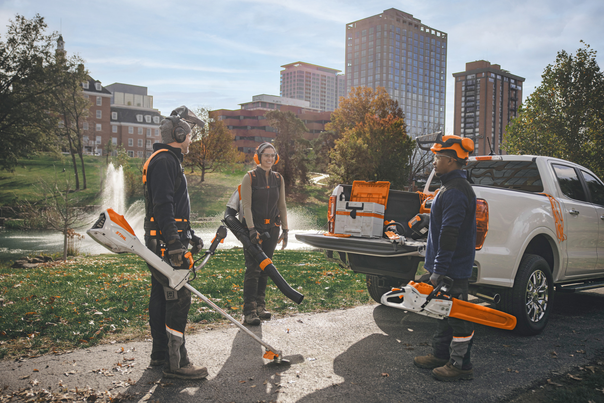 Um grupo de paisagistas profissionais, reunidos à volta dos seus veículos, a prepararem-se para trabalhar com ferramentas elétricas a bateria da STIHL. 