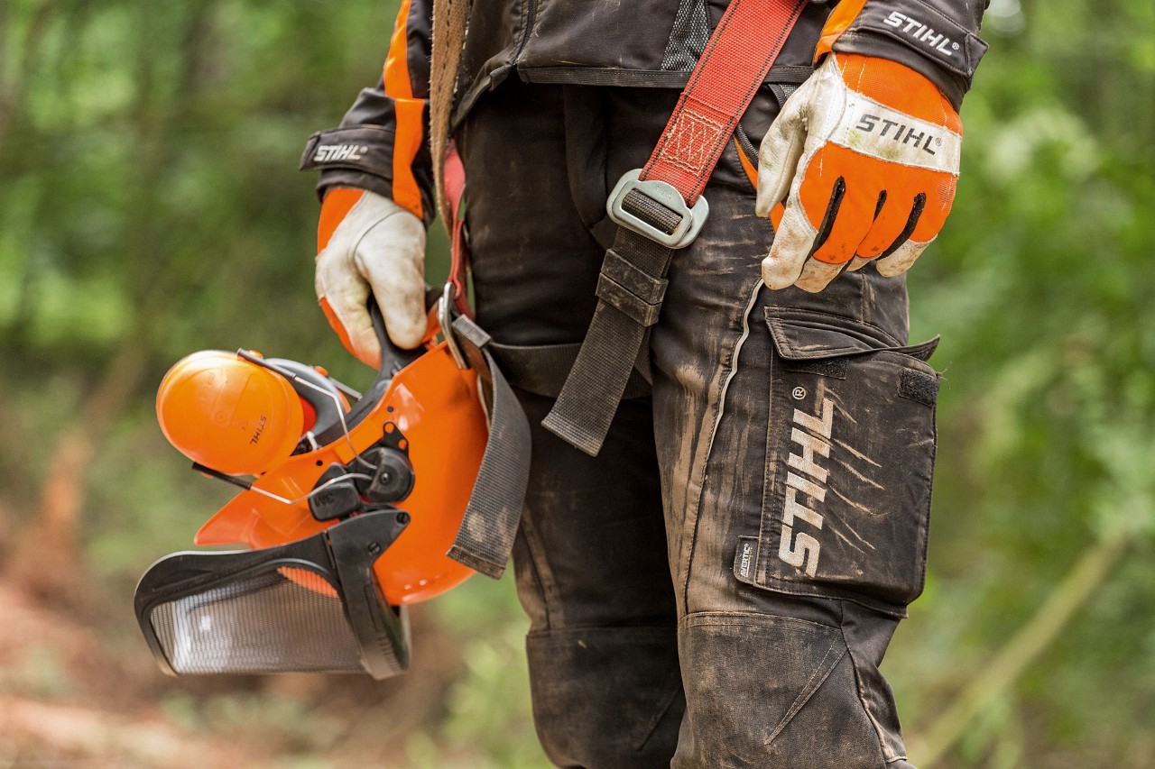 Categorias de proteção de motosserras: uma pessoa com calças e luvas de proteção da STIHL, com um capacete na mão 