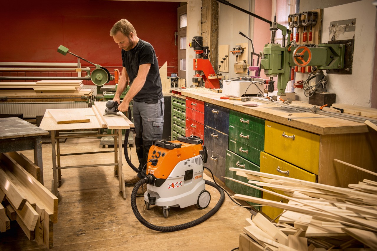 Categorias de extração de pó: homem a usar um aspirador STIHL SE 133 ME numa oficina enquanto trabalha tábuas de madeira