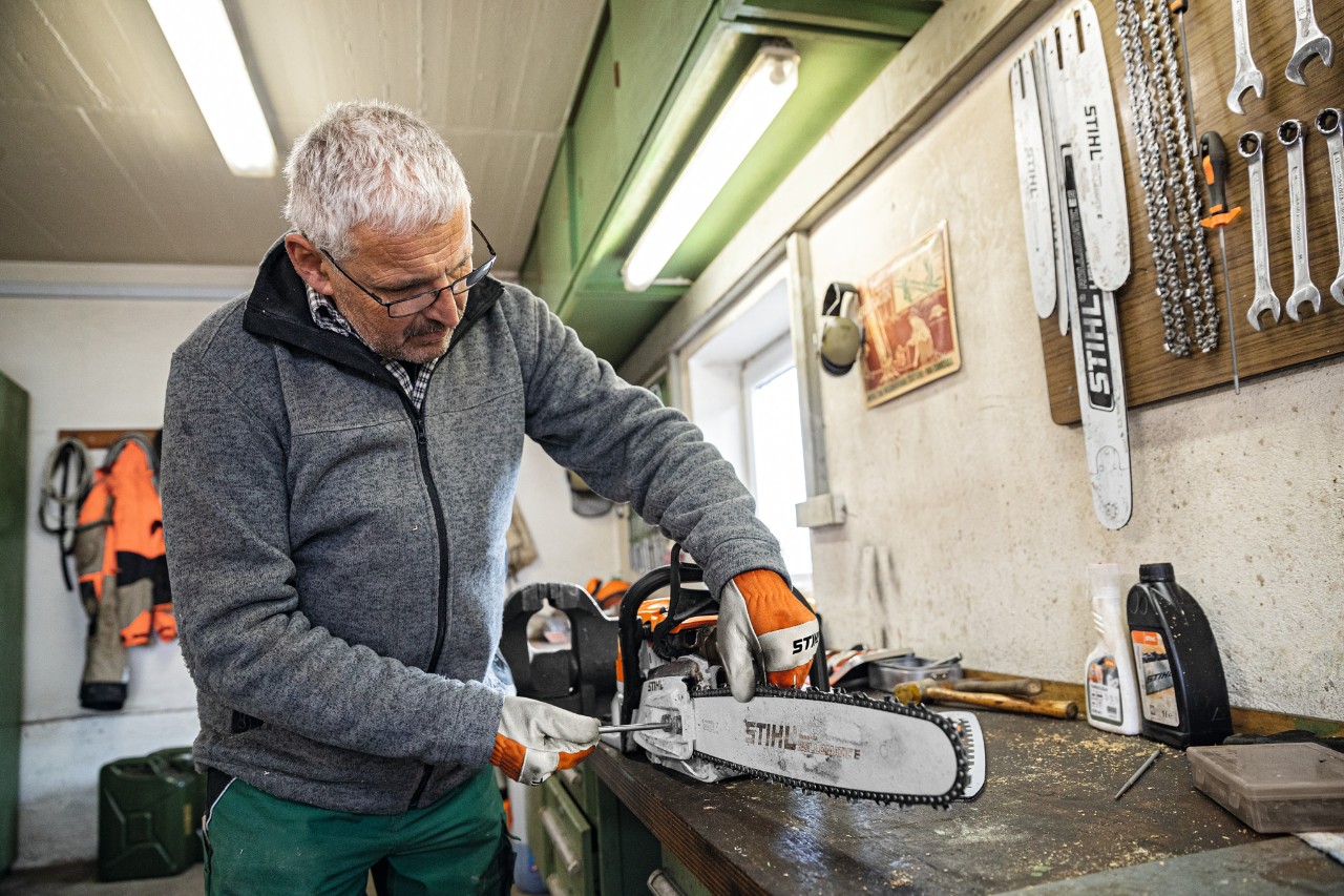 Um homem numa oficina a trabalhar numa motosserra com barra-guia STIHL Rollomatic E 