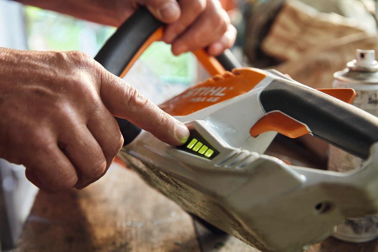 Uma pessoa verifica o nível de carga do aparador de sebes sem fios STIHL HSA 45.