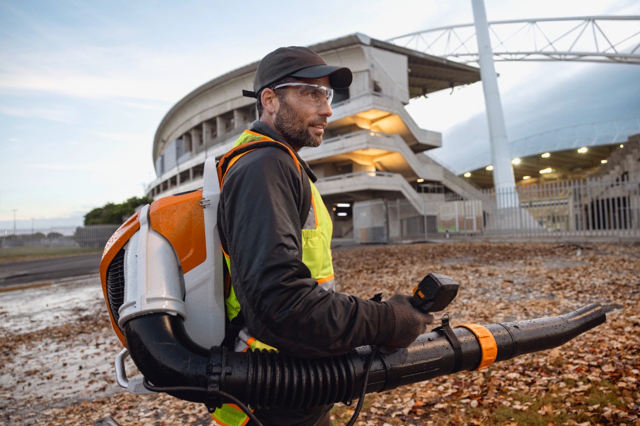 Ao fim da noite, uma pessoa está a limpar folhas e detritos de um estádio com o soprador de folhas sem fios ALLPRO STIHL BRA 600.