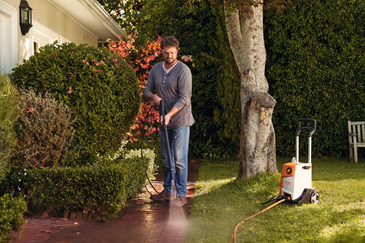 Homem a limpar pedras de calçada à frente da sua casa com uma máquina de limpeza de alta pressão STIHL RE 110
