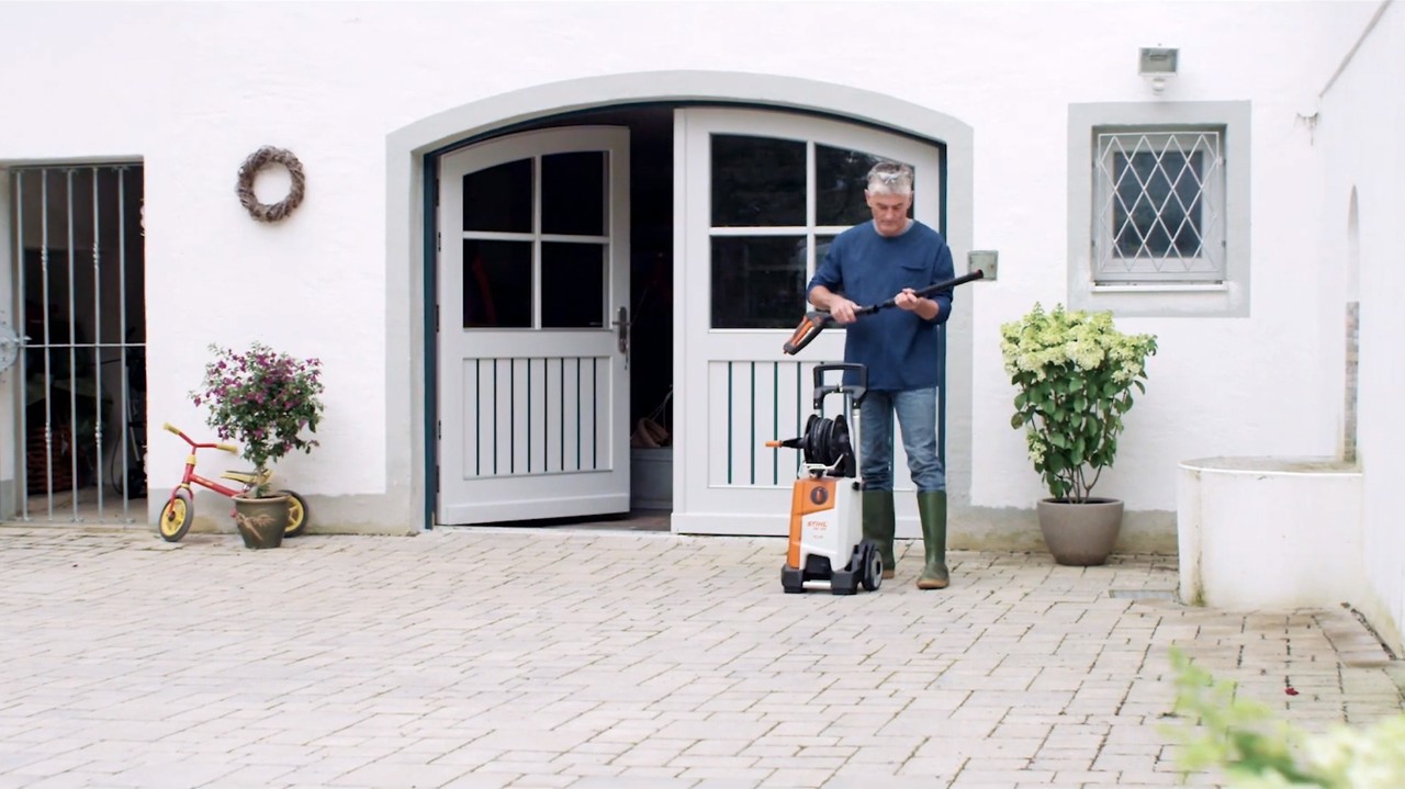 Um homem à frente de uma casa branca a preparar uma máquina de limpeza de alta pressão STIHL para limpar a fachada