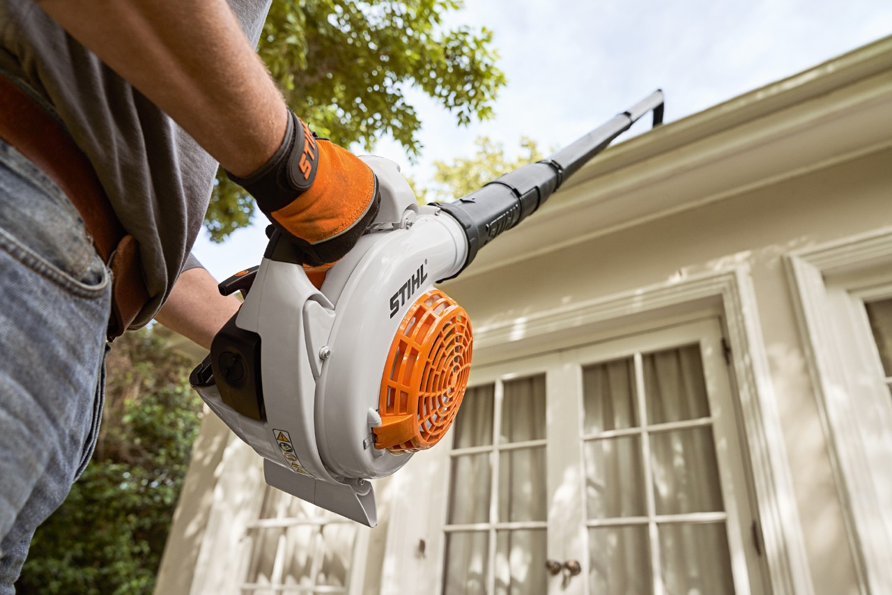Vista para cima de um kit de limpeza de algerozes e de um soprador de folhas STIHL a serem utilizados para limpar algerozes numa casa branca