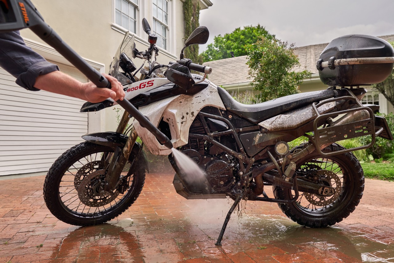 Uma moto na entrada de uma casa branca, a ser limpa com uma máquina de lavagem de alta pressão STIHL RE 130 Plus