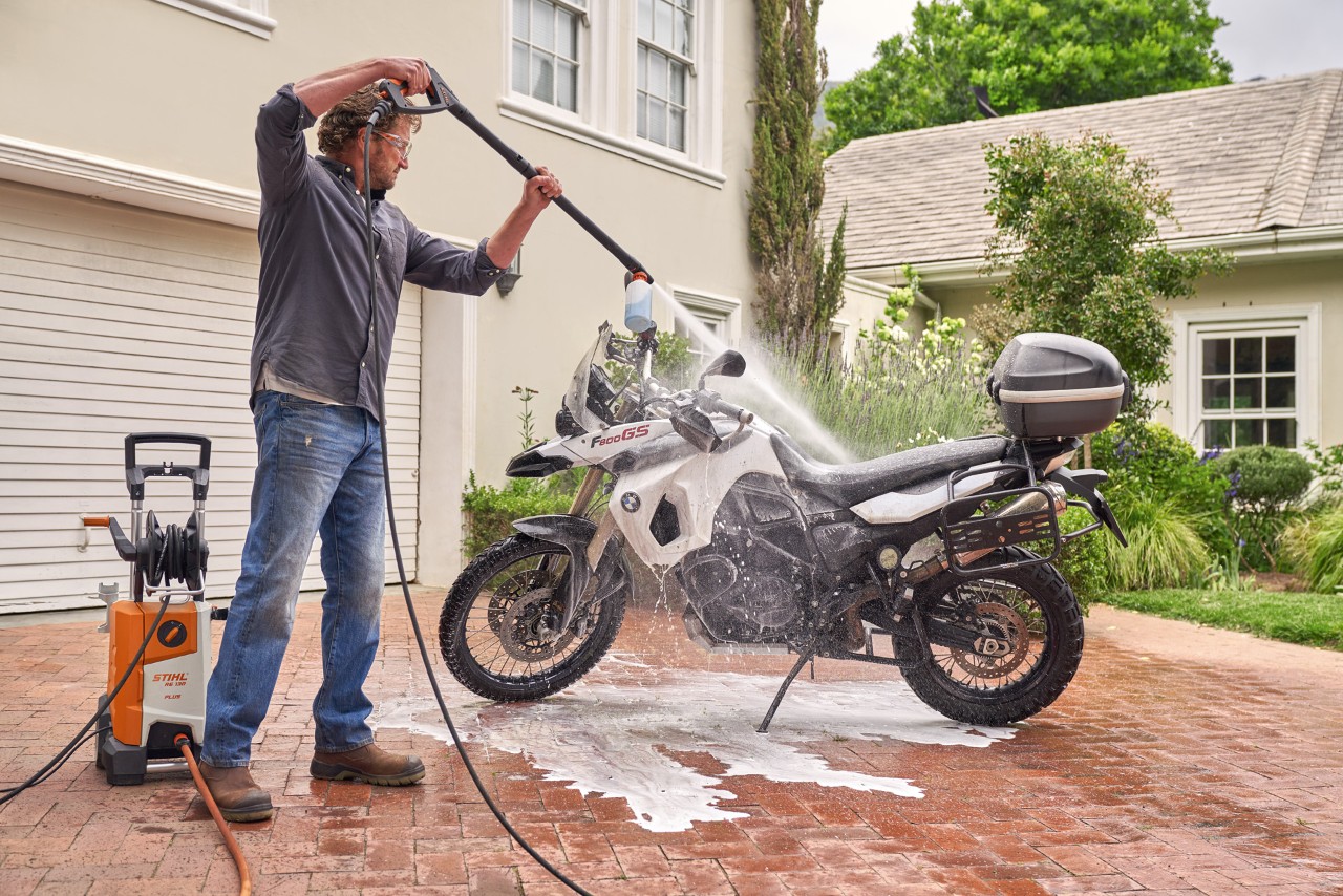 Um homem a usar a máquina de lavagem de alta pressão STIHL RE 130 Plus para pulverizar champô auto sobre uma moto