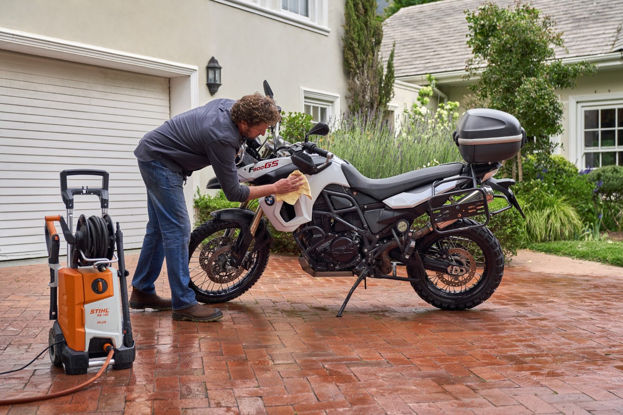 Homem a secar uma moto com um pano de camurça, com uma máquina de lavar de alta pressão STIHL RE 130 Plus ao seu lado