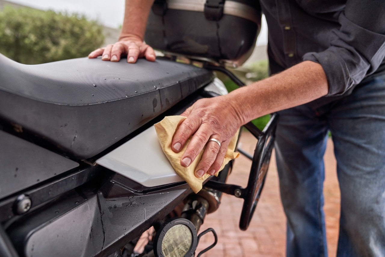 Imagem ampliada de cera a ser aplicada com um pano macio numa área pintada de uma moto - lavar moto a alta pressão