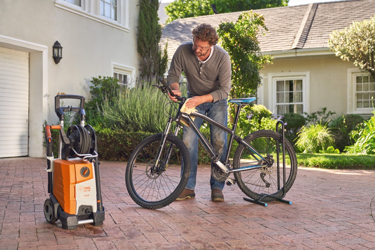 Um homem a secar uma bicicleta com um pano, com uma lavadora de alta pressão STIHL RE 130 plus ao lado