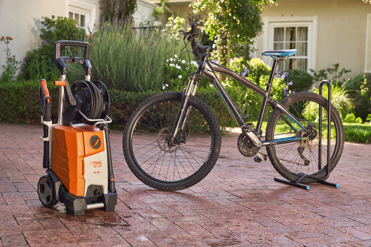 Uma bicicleta acabada de lavar à frente de uma casa junto a uma lavadora de alta pressão STIHL RE 130 plus