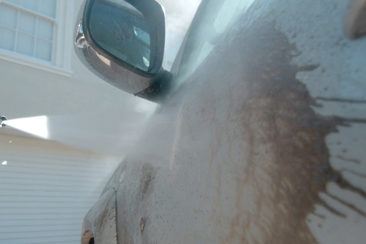 Imagem ampliada de uma porta de carro suja a ser lavada com uma máquina de lavar de alta pressão
