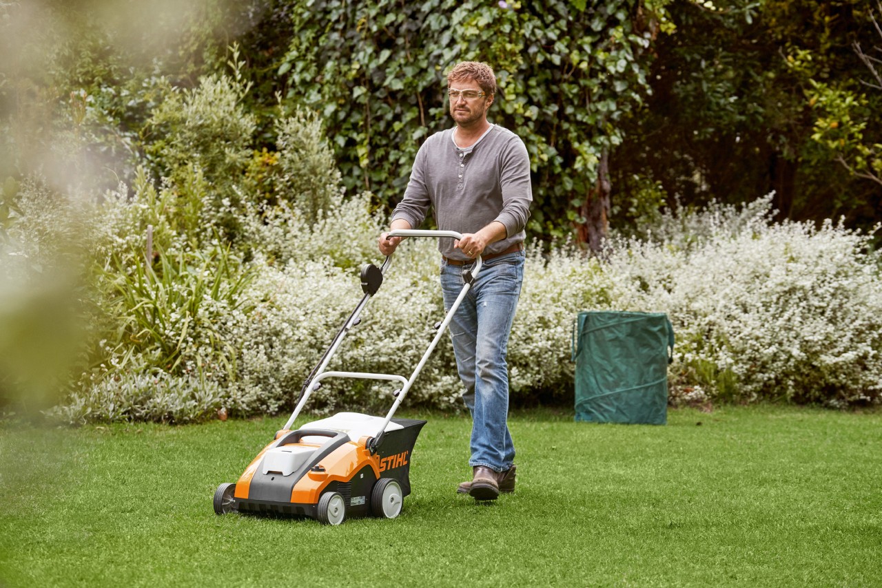 Um homem escarifica o relvado verde com um arejador de relva a bateria STIHL RLA 240