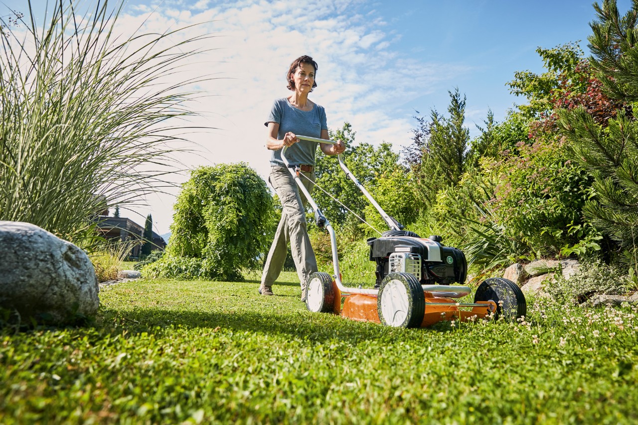 Mulher a aplicar mulch com um corta-relva de mulching a gasolina STIHL RM 2 R num terreno verde