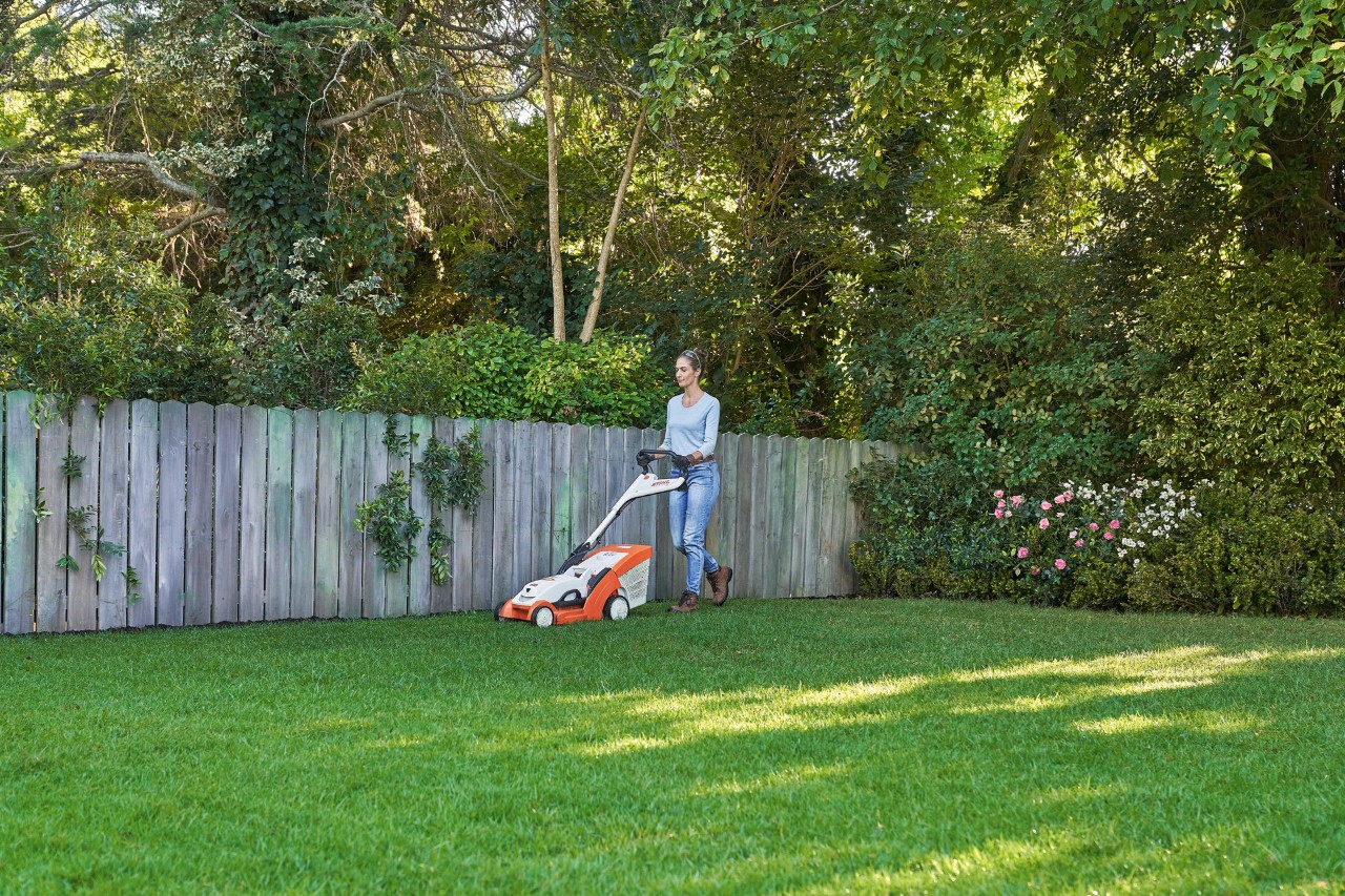Uma mulher corta uma área relvada verde frente a uma vedação de madeira com o corta-relva a bateria STIHL RMA 339 C.