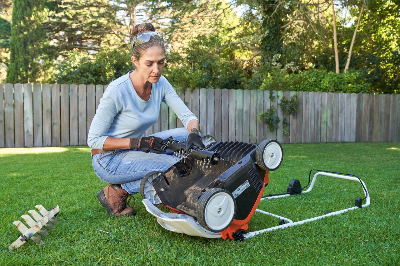 Uma mulher com luvas de trabalho substitui a unidade de escarificação do arejador de relva a bateria STIHL RLA 240