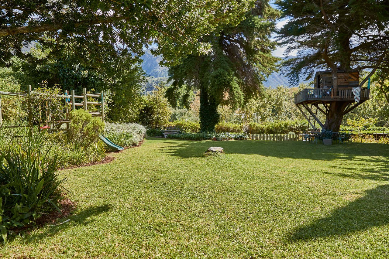 Bom exemplo de como aplicar relva num grande relvado com árvores, canteiros de flores e uma casa na árvore.