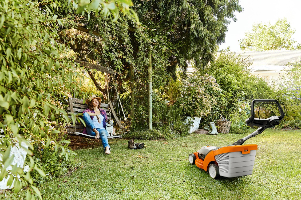 Uma mulher relaxa num balouço de jardim ao lado de um corta-relva a bateria STIHL RMA 339 num espaço verde