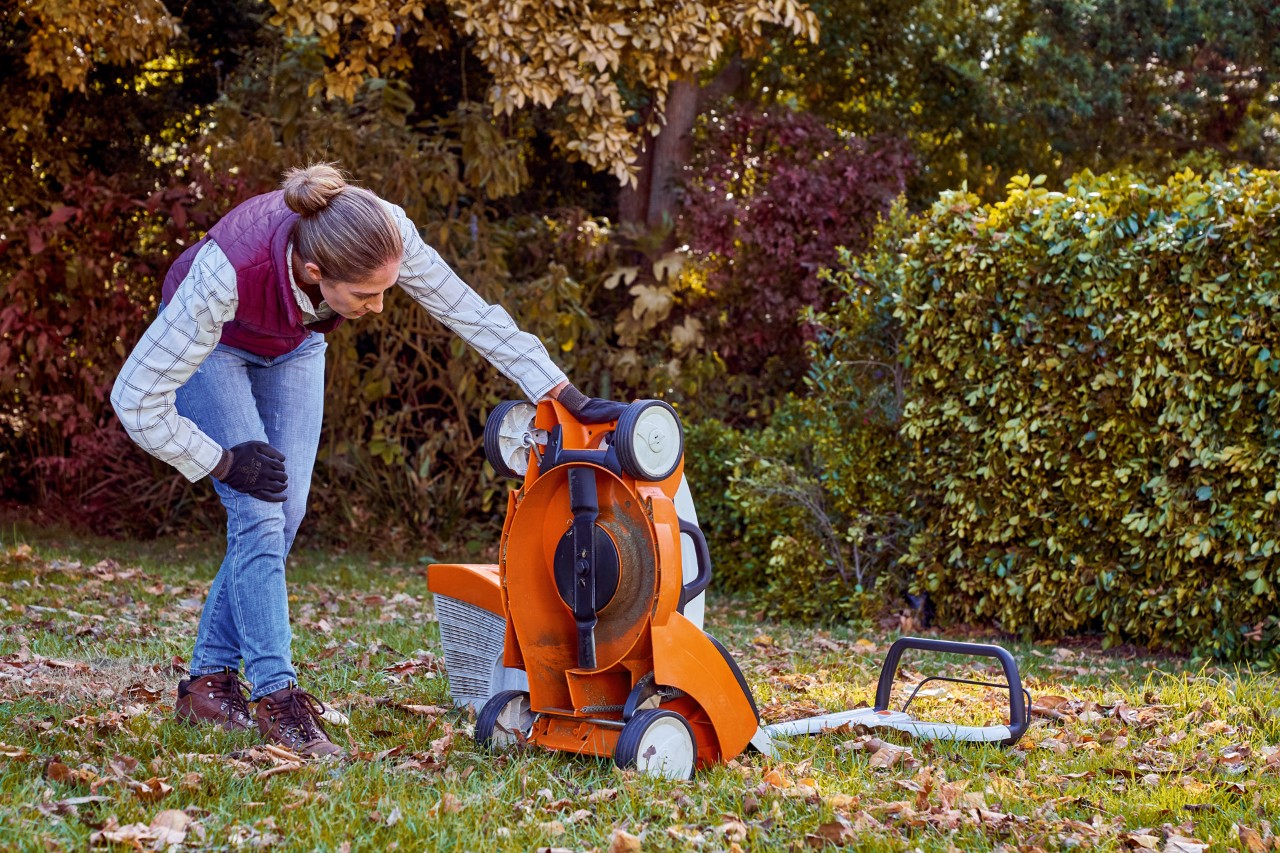 Mulher aplica os cuidados com a relva no outono ao inspecionar a parte inferior de um corta-relva STIHL RMA 339 C 