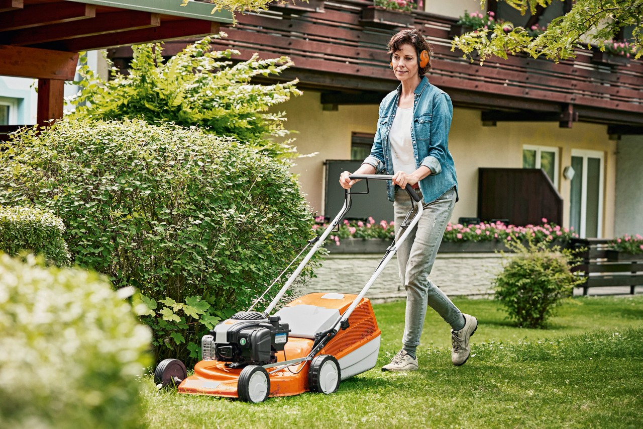 Uma mulher a utilizar um corta-relva a gasolina STIHL RM 243 T no espaço verde, à frente de uma casa