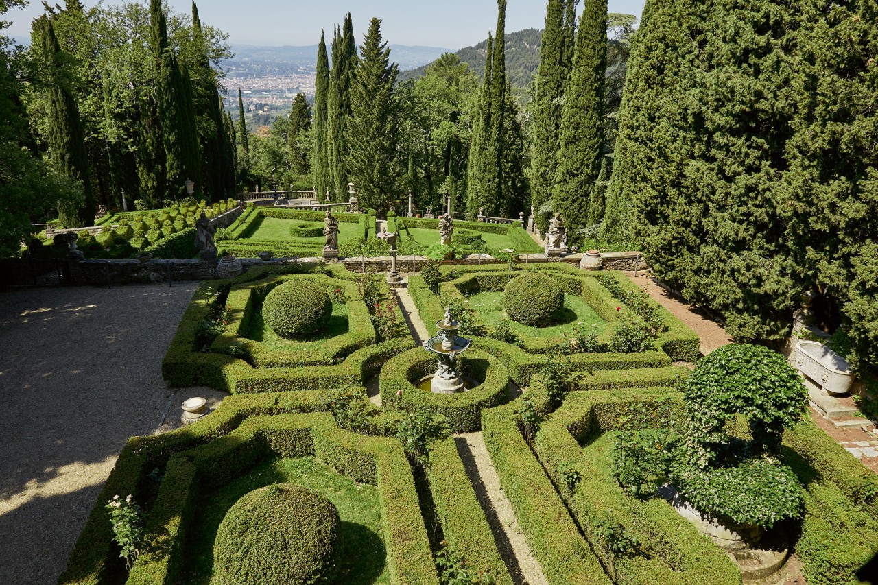 Vista de um espaço verde topiário formal com sebes de formas geométricas e bolas de topiaria. 