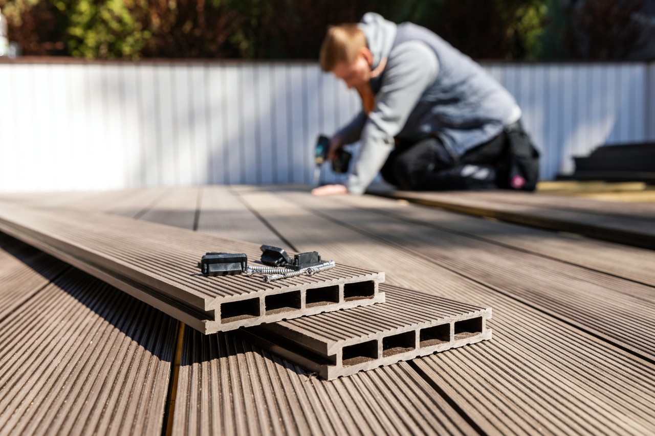 Design de terraços: alguém a assentar um chão de WPC num terraço à frente de uma vedação branca