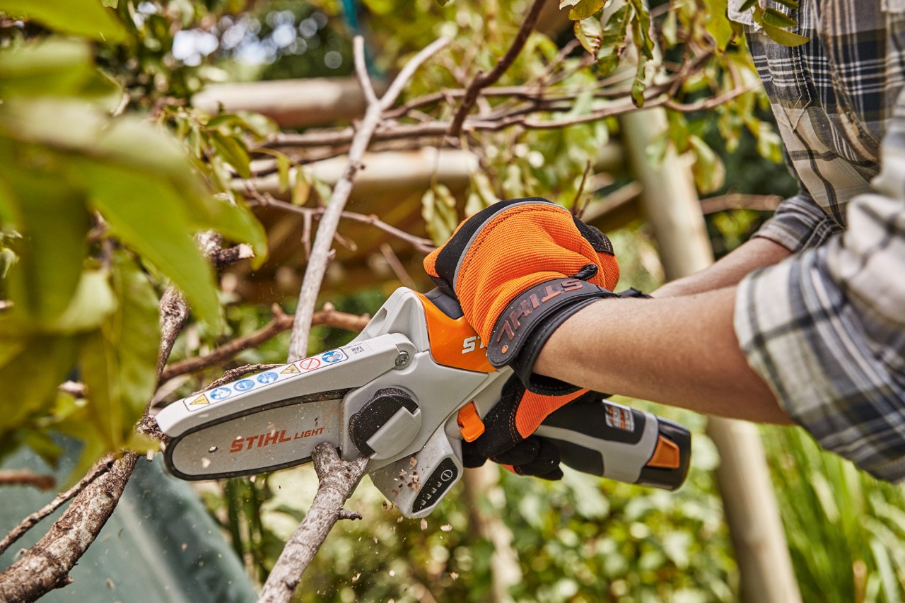 Tarefa de jardinagem no outono: alguém apara ramos com luvas e uma minipodadora de corrente a bateria STIHL GTA 26 