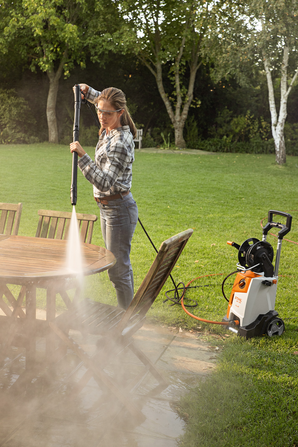 Uma mulher usa a lavadora de alta pressão STIHL RE 130 PLUS no exterior para limpar mobiliário de jardim