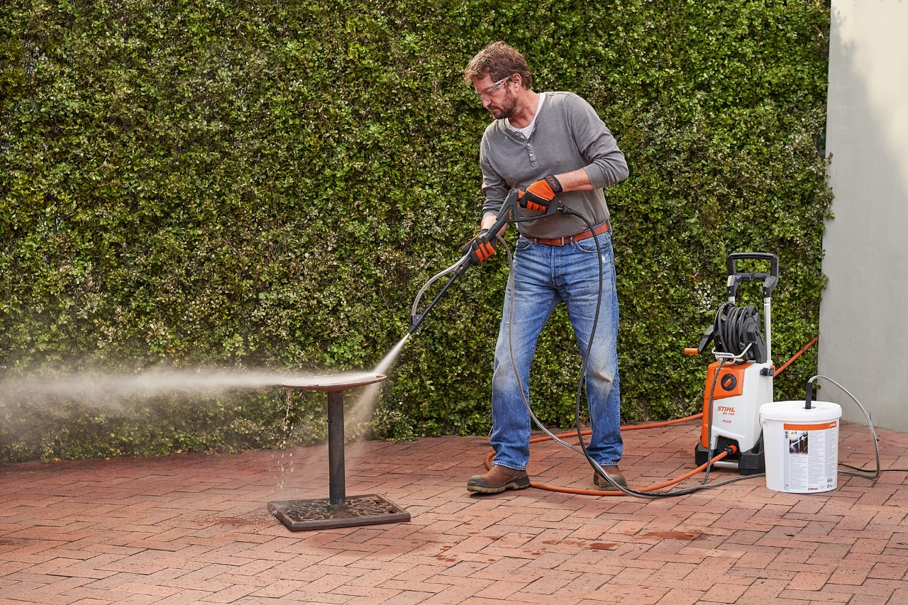 Um homem à frente de uma garagem a usar a injeção de areia húmida com uma máquina de limpeza de alta pressão STIHL RE 130 PLUS
