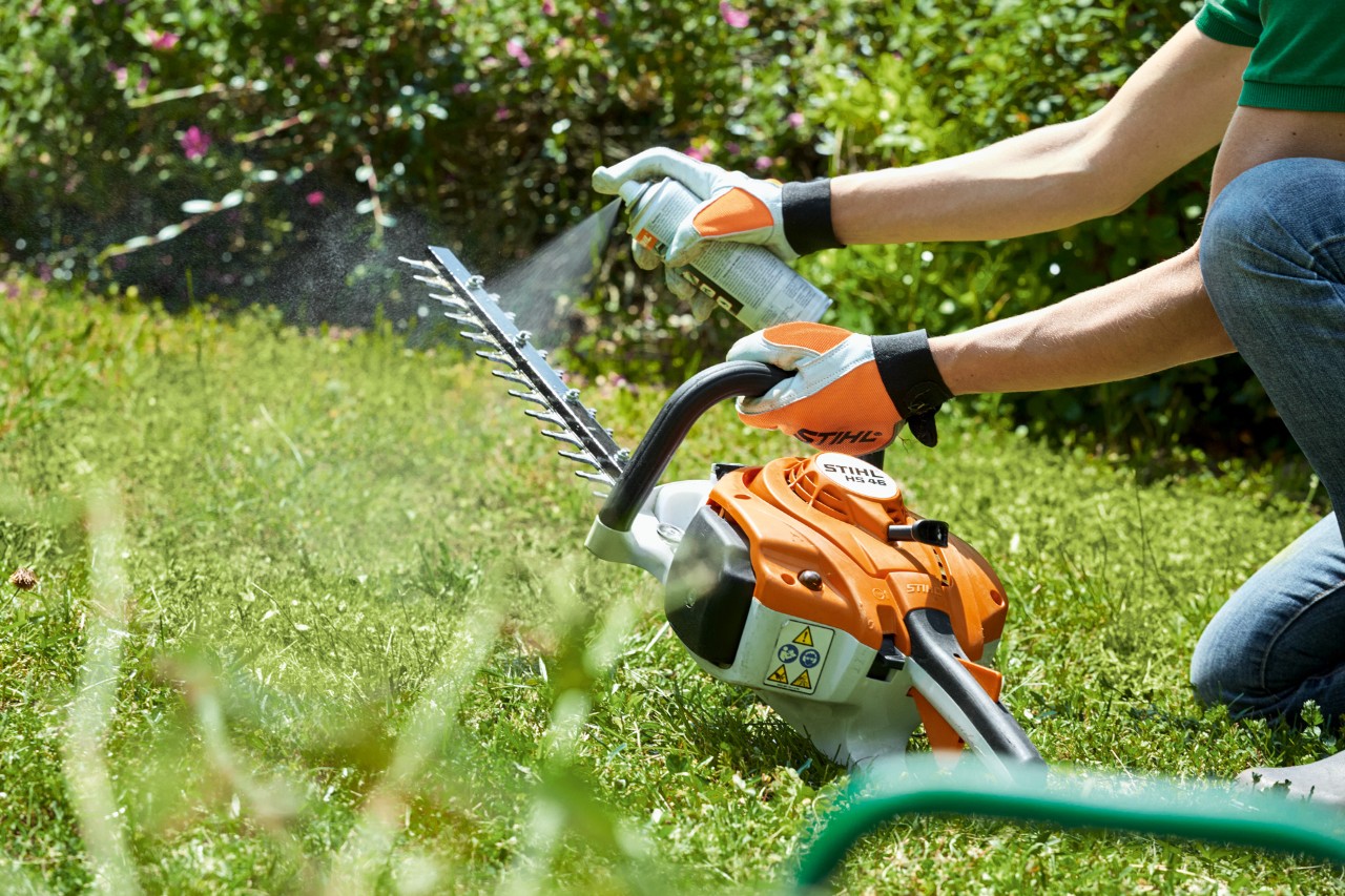  Uma podadora de sebes a gasolina STIHL HS&nbsp;82&nbsp;T a ser pulverizada num relvado verde para a limpar