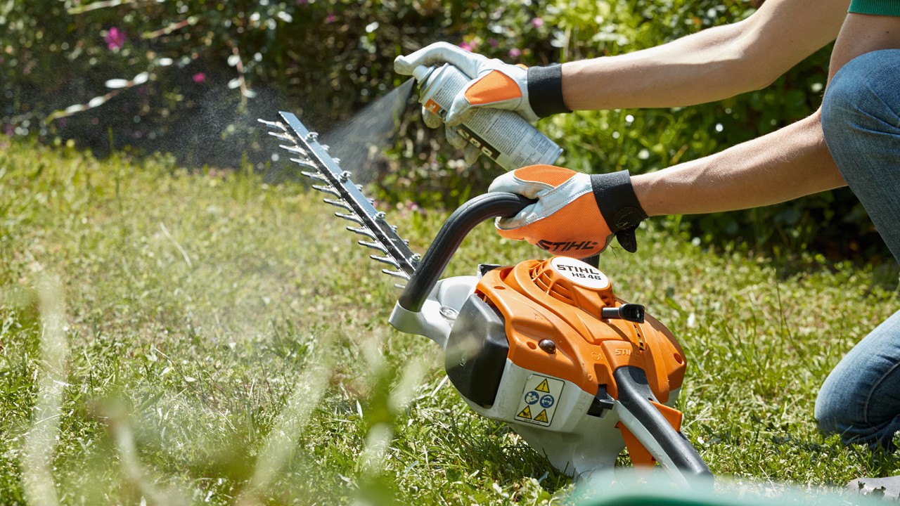 Boa prática de como limpar um corta-sebes a gasolina STIHL HSA 82 T: num relvado e a pulverizar solvente de resina.