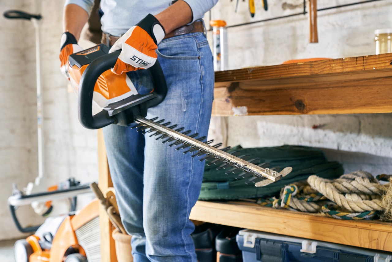 Uma pessoa procede à manutenção do corta-sebes a bateria STIHL HSA 56, à frente de uma bancada de trabalho 