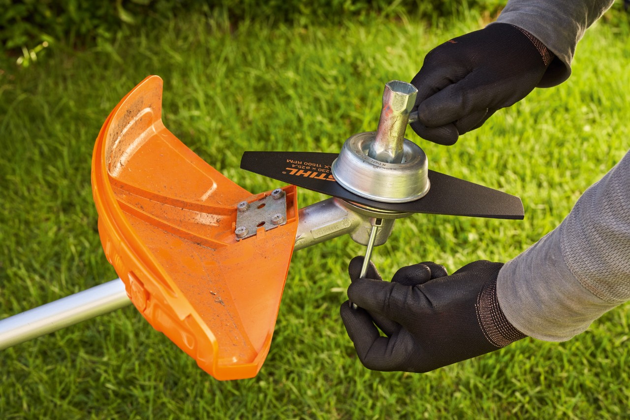 Uma pessoa com luvas de proteção postas verifica a lâmina de corte de uma  roçadeira STIHL a motor