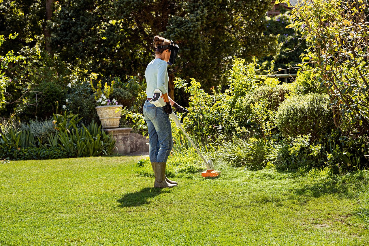 Uma mulher apara a erva alta dos rebordos de um jardim usando uma aparadora a bateria STIHL FSA 57