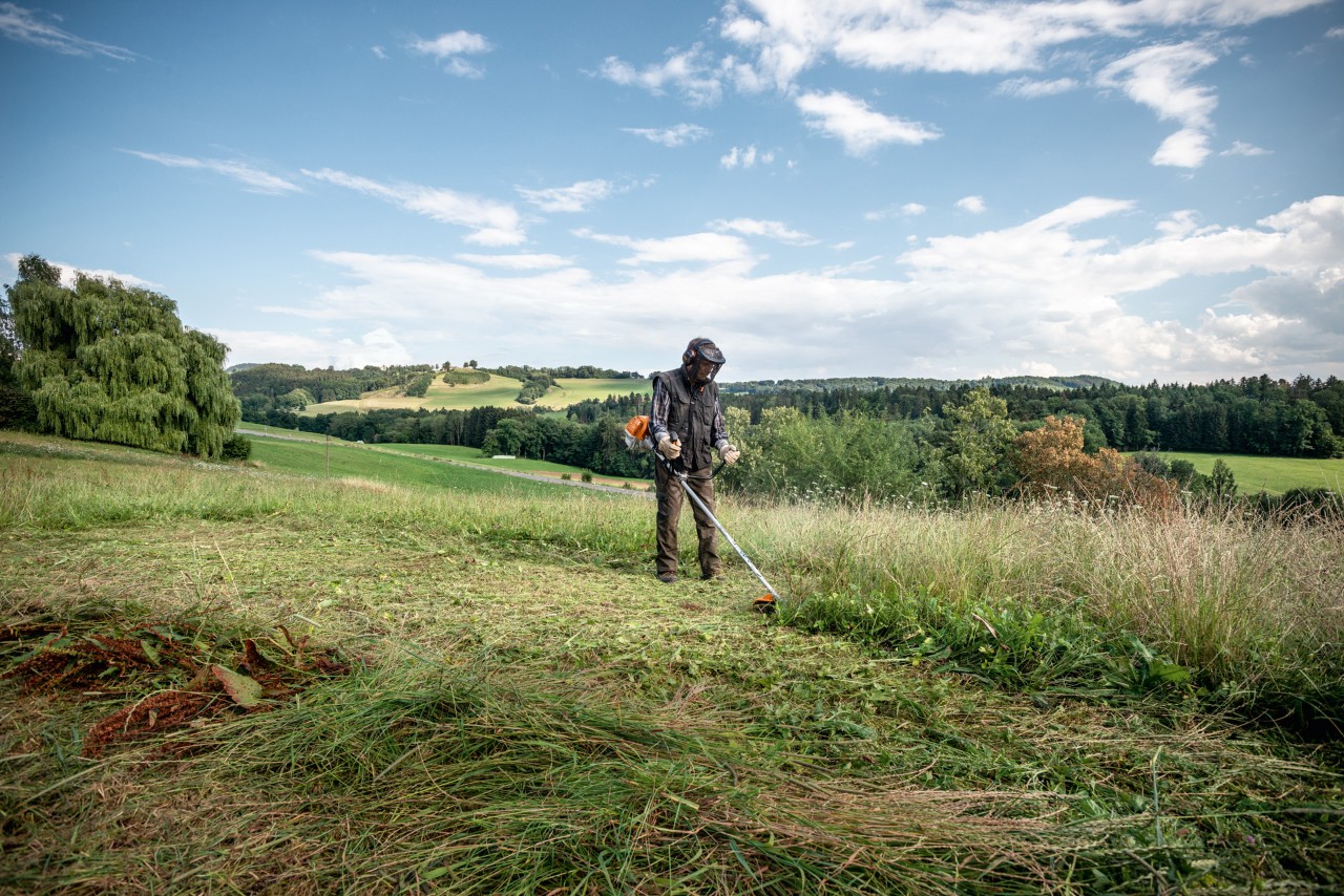 Uma pessoa a cortar erva numa extensa área de terreno plano demonstra como usar uma motorroçadora STIHL 