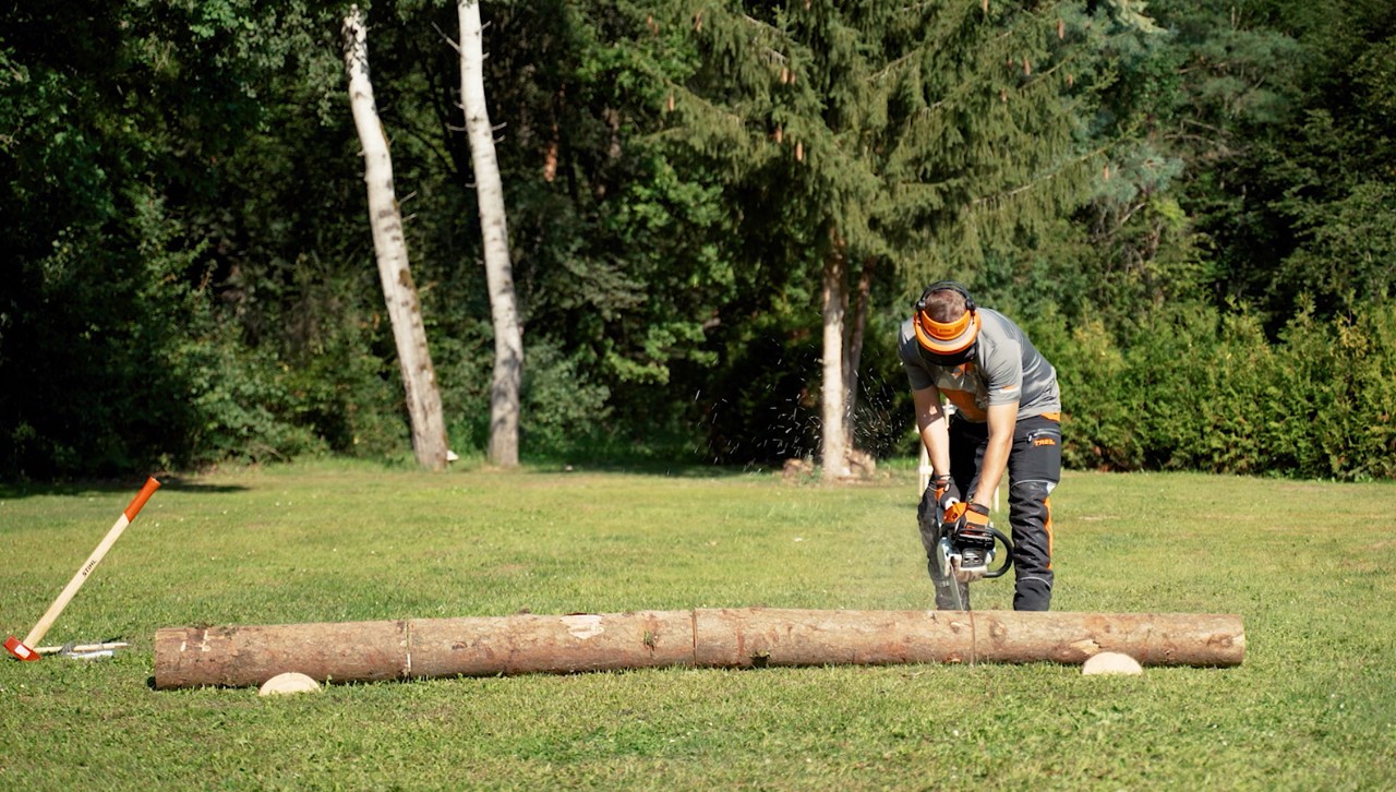 Uma pessoa com equipamento de proteção usa uma motosserra STIHL para transformar o tronco de uma árvore em lenha