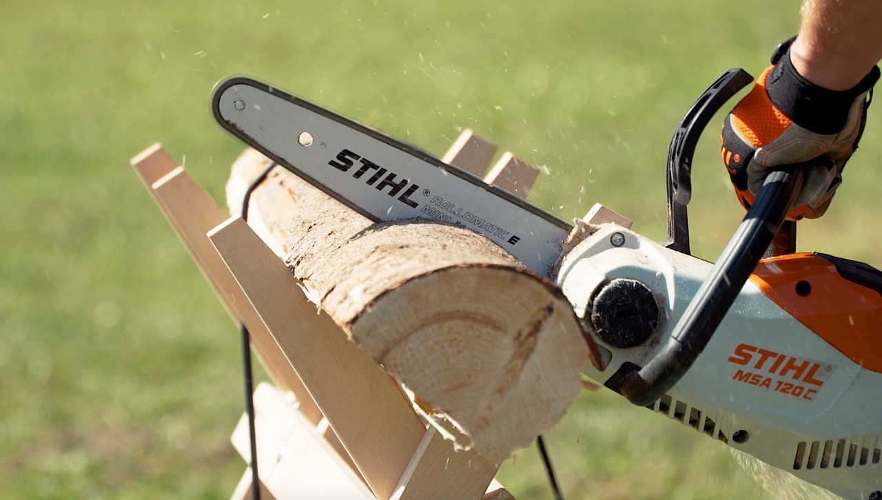 Um tronco num cavalete é transformado em lenha com uma motosserra STIHL MSA 120 C