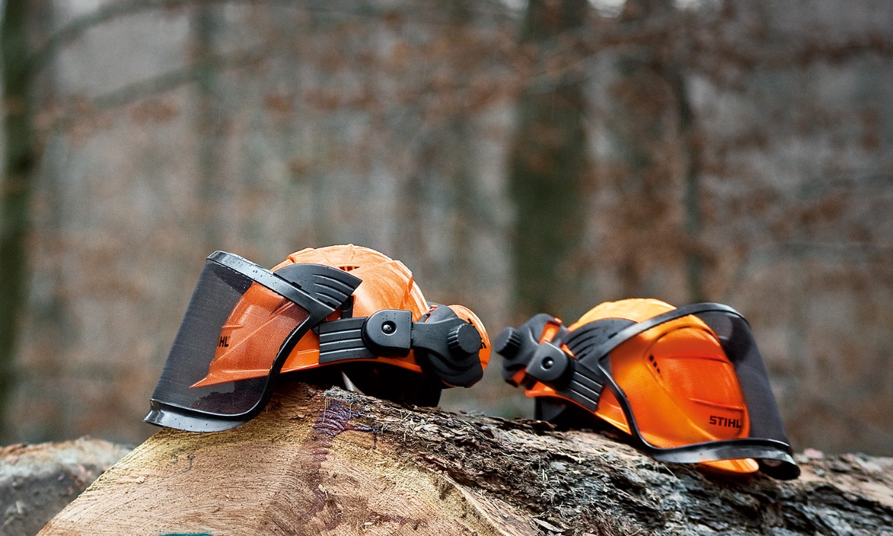 Dois conjuntos de capacete STIHL ADVANCE pousados sobre troncos de árvores numa floresta - parte de EPI para motosserra 