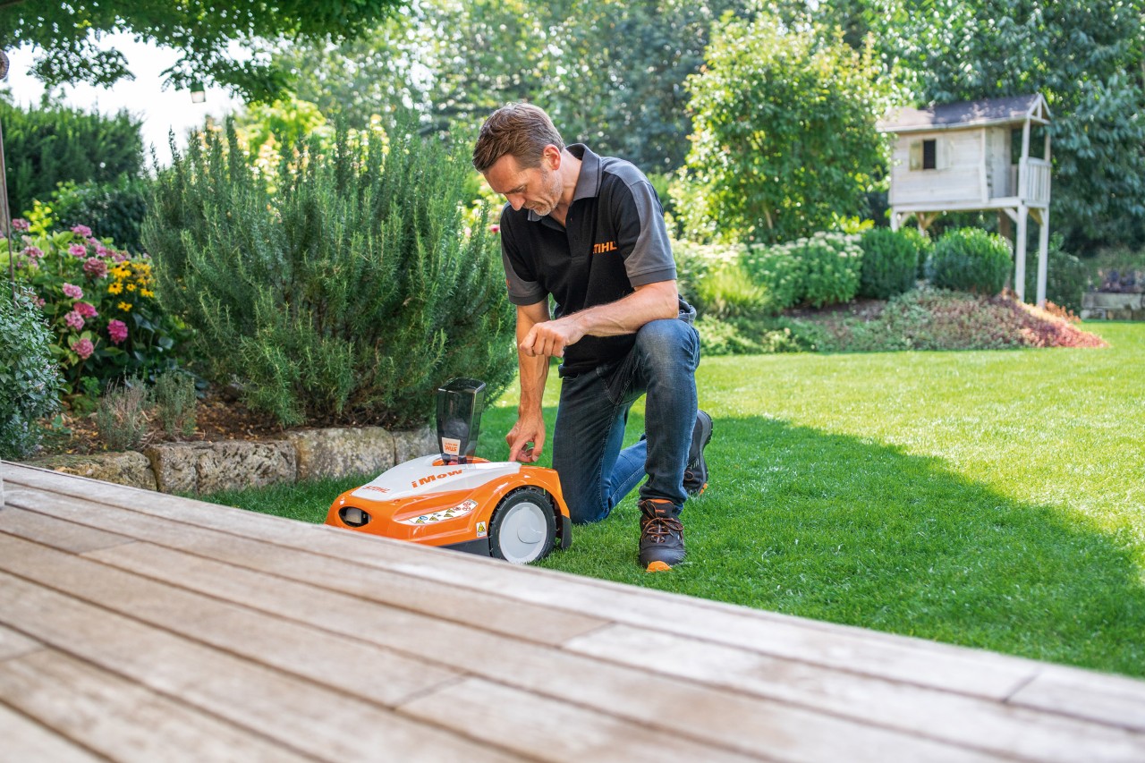 Um concessionário STIHL a usar o painel de controlo de um robot corta-relva STIHL iMOW® 422 num jardim