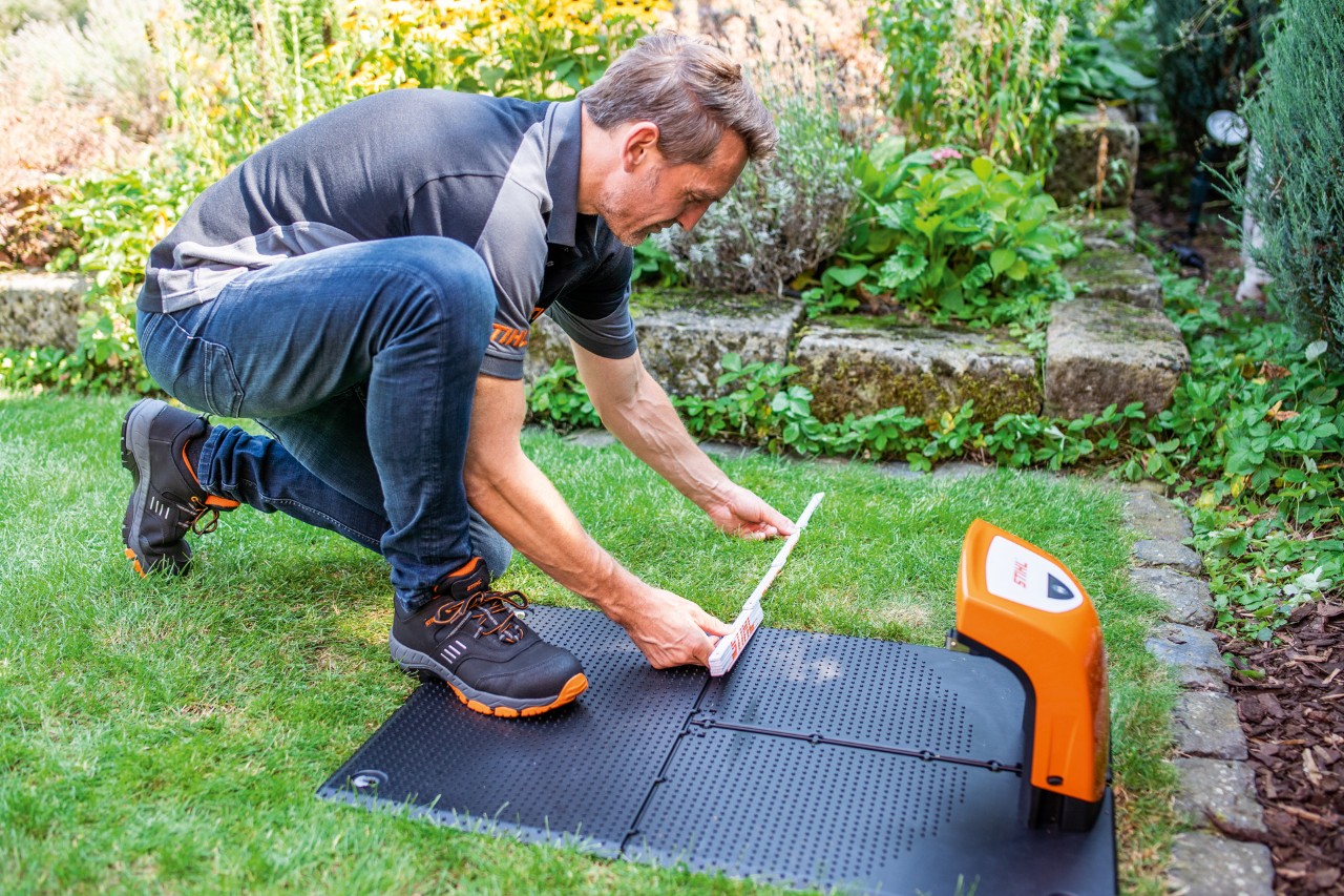 Um concessionário STIHL a instalar a estação de carga para um robot para cortar relva STIHL iMOW® 422 num jardim