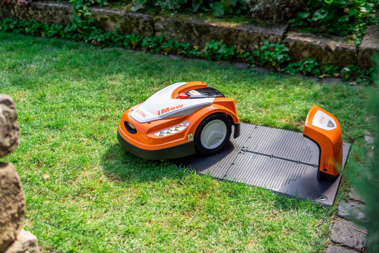 Um robot corta-relva STIHL iMOW® ao lado da respetiva estação de carga num relvado verde