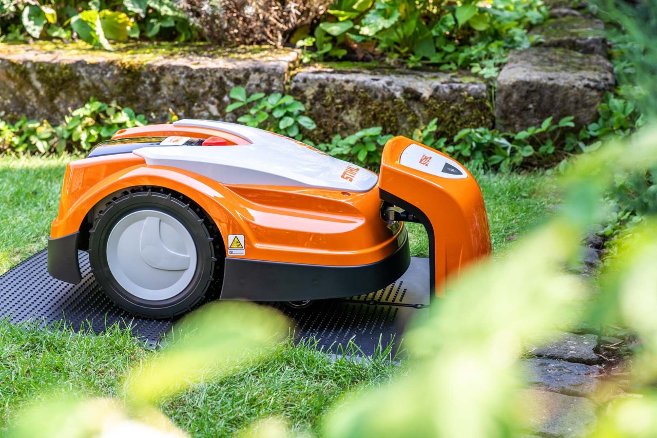 Um robot corta-relva no inverno, num jardim, a recarregar na estação de carga