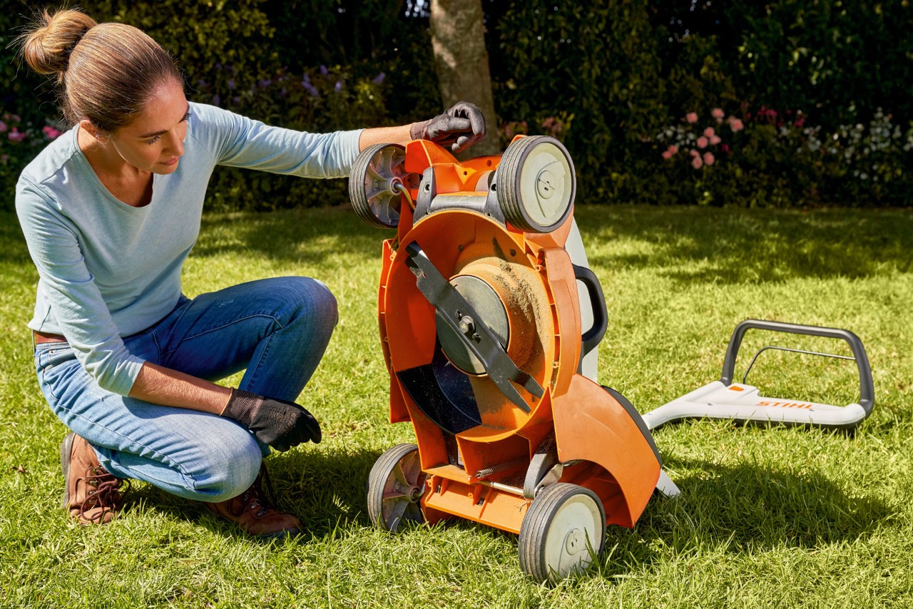 Uma mulher num jardim espreita por baixo do seu corta-relva a bateria STIHL RMA 339C