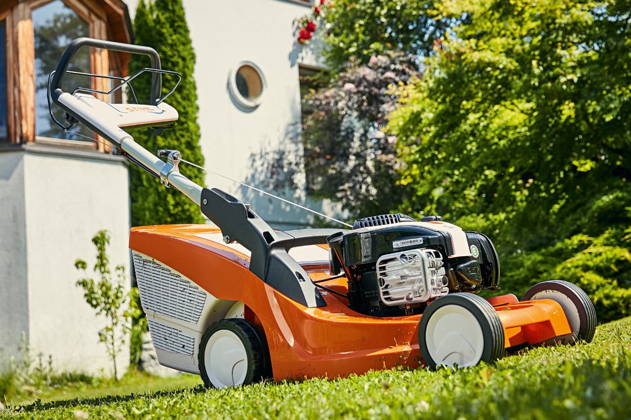 Corta-relva a gasolina STIHL RM 443 T num relvado verde em frente a uma casa 