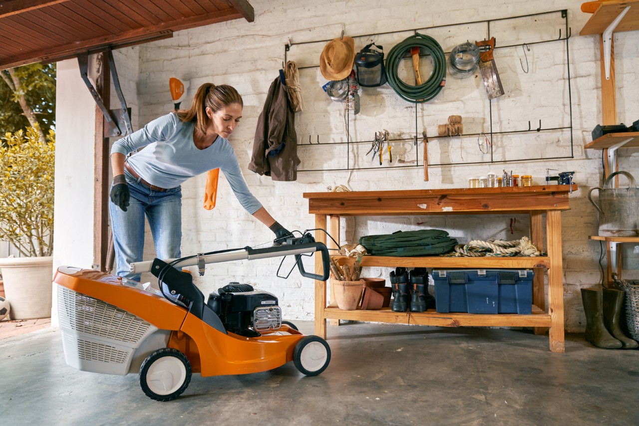 Uma mulher numa garagem prepara o corta-relva a gasolina STIHL RM 448 TC para o inverno antes de o armazenar