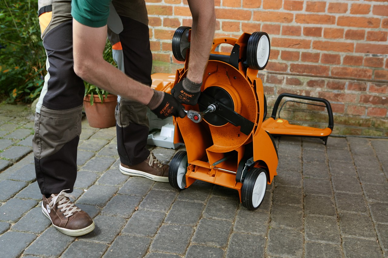 Uma pessoa de luvas a remover a lâmina de um corta-relva STIHL RM virado ao contrário