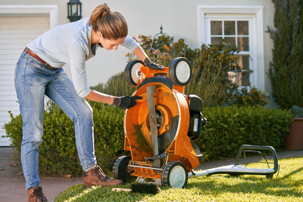 Uma mulher exemplifica como limpar um corta-relva ao usar uma espátula na parte inferior de um STIHL RM 448 T-C