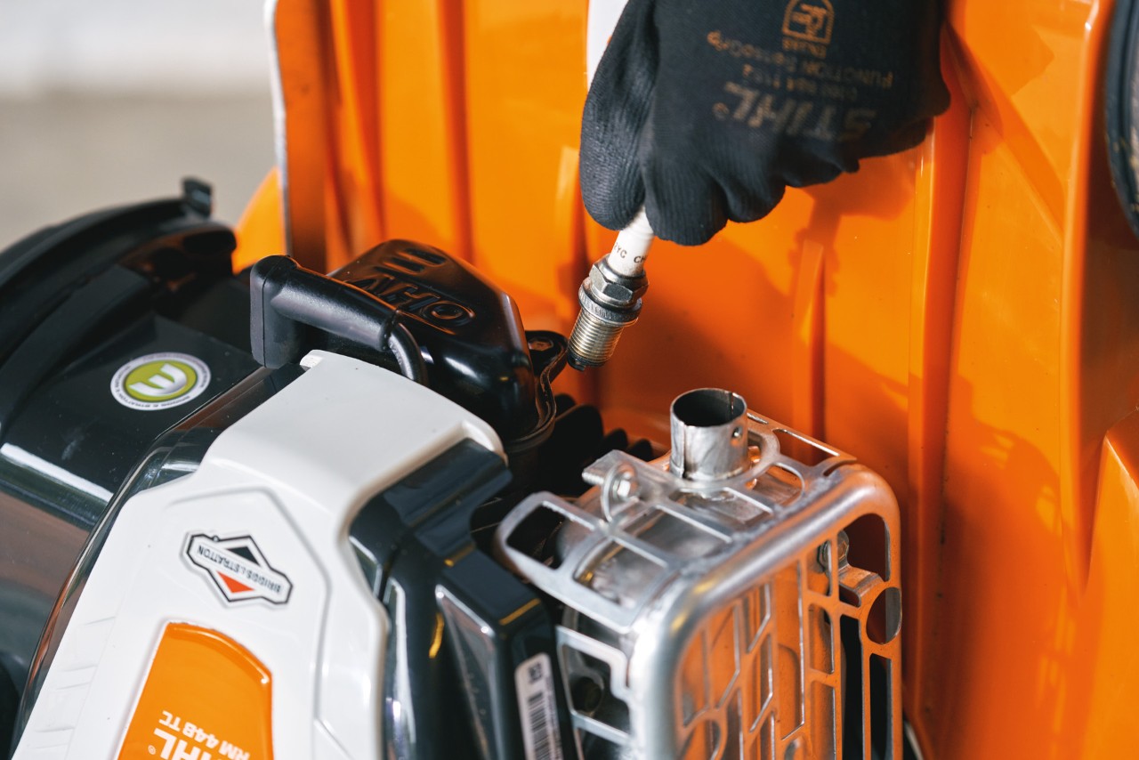 Imagem ampliada de alguém a remover uma vela de ignição de um corta-relva STIHL posto ao alto.