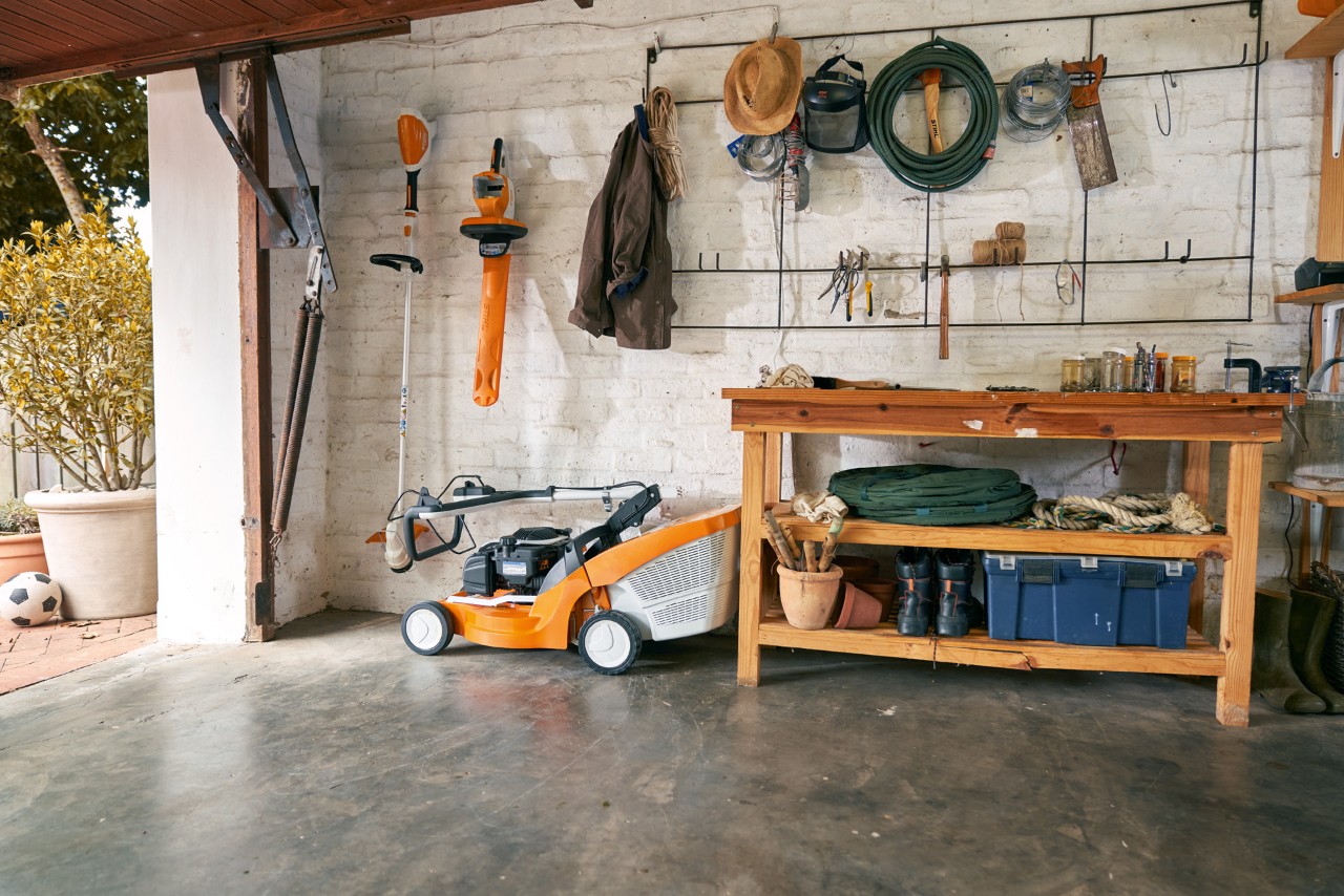 Um corta-relva a bateria STIHL RMA 339 C armazenado em segurança numa garagem com bancada de trabalho e ferramentas.