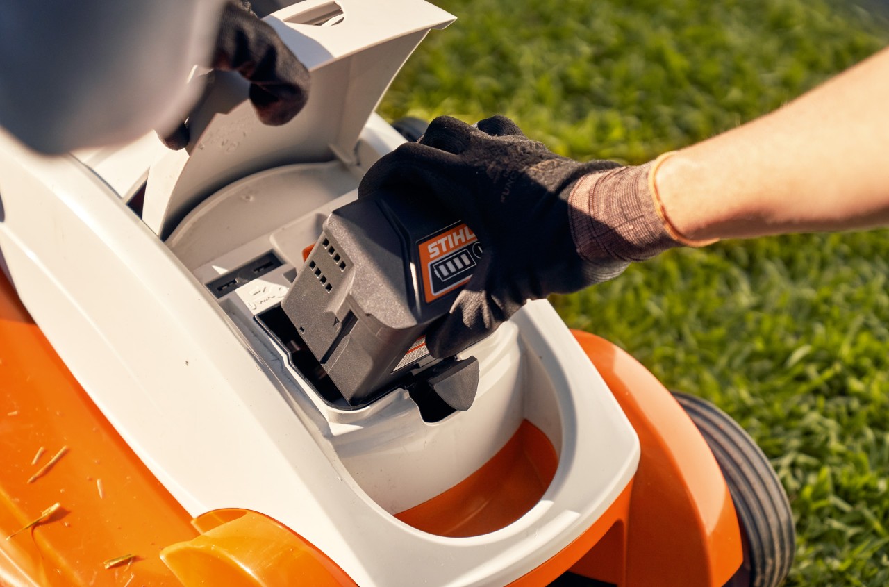 Pessoa remove a bateria de um corta-relva sem fio STIHL RMA 339C para prepará-lo para o inverno
